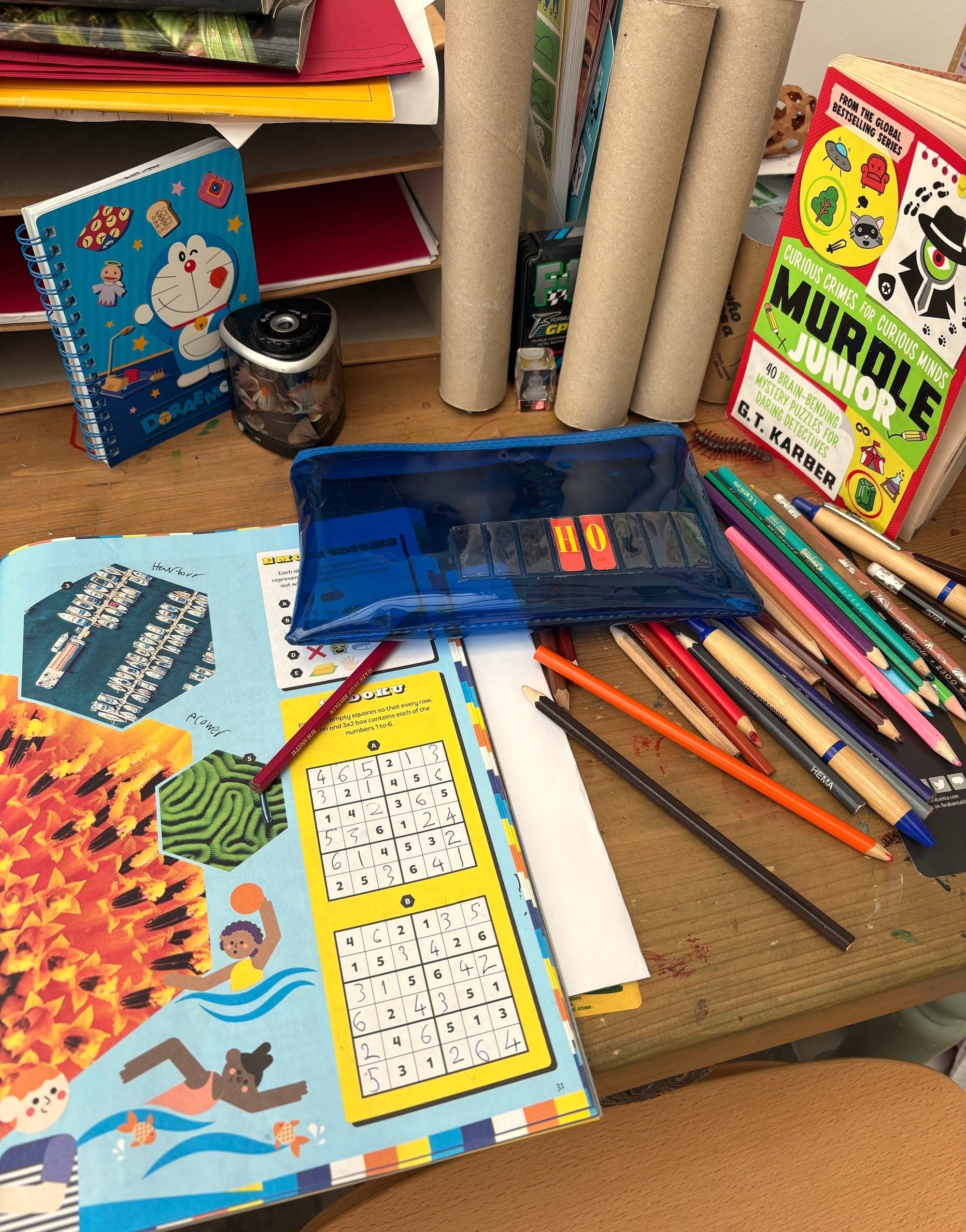 A desk with a puzzle book, crayons and pencil case