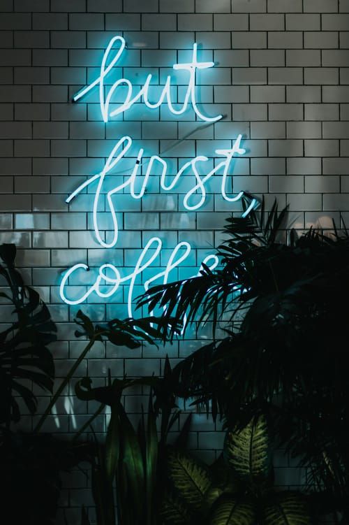 A blue neon sign saying 'But first coffee'